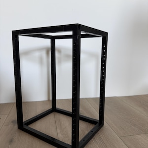 May include: A black rectangular frame constructed from four vertical pillars and eight horizontal connecting bars. The vertical pillars feature a series of evenly spaced circular holes along their length, creating a modular open-structure rack.