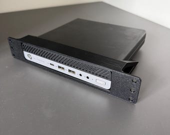 May include: A black HP EliteDesk mini computer mounted in a black 3D-printed rack mount bracket. The front panel features a silver faceplate with two USB ports, a USB-C port, audio jacks, and a power button, all framed by a textured black mount.