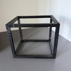 May include: A black, open-frame cube structure constructed from modular components. The four vertical corner posts feature a series of evenly spaced circular holes along their length, while the horizontal connecting bars are solid and smooth.