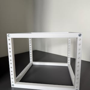 May include: A white, cubic, open-frame rack structure constructed from rigid material. The frame features vertical supports with a series of evenly spaced circular holes along the front edges, secured at the corners with visible metallic screws.