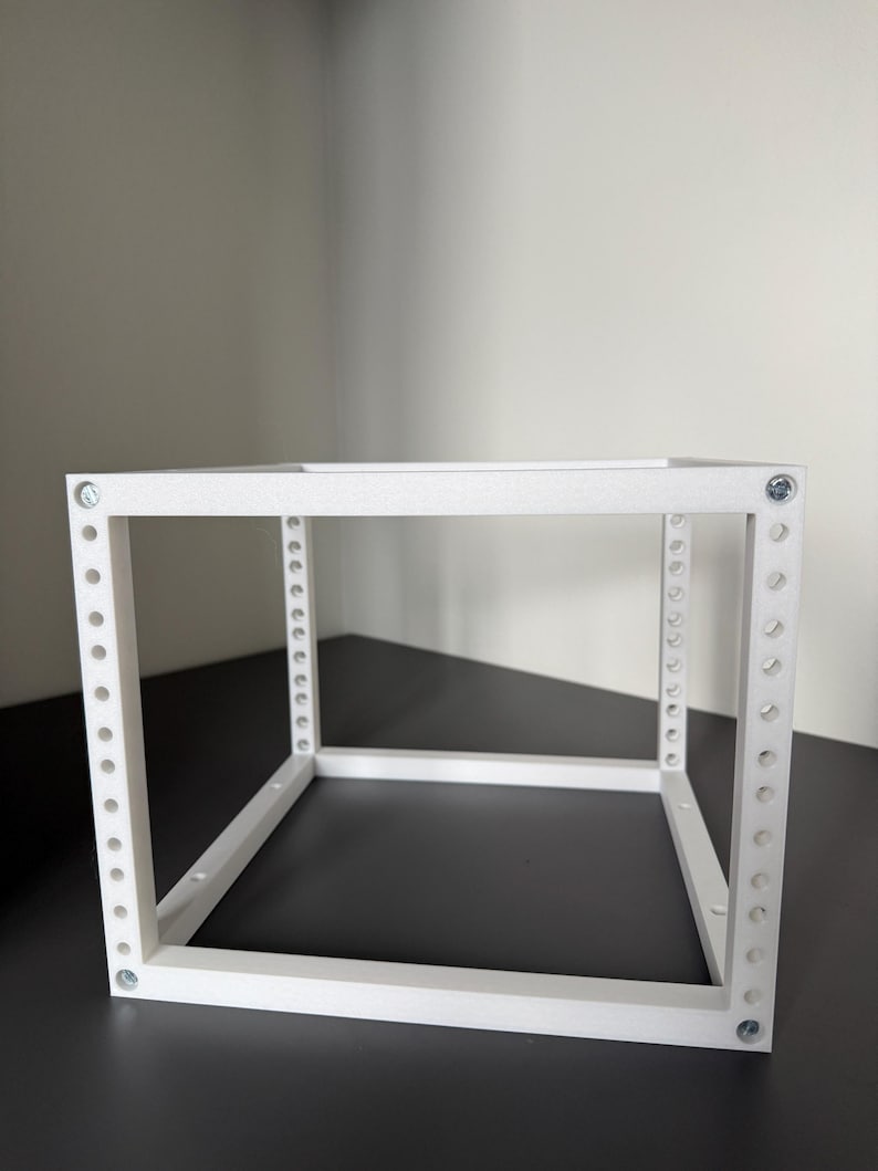 May include: A white, cubic, open-frame rack structure constructed from rigid material. The frame features vertical supports with a series of evenly spaced circular holes along the front edges, secured at the corners with visible metallic screws.