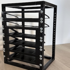 May include: A black modular storage rack featuring a vertical frame with five horizontal shelves. The structure is assembled with silver-colored metal screws visible along the side panels, creating a grid-like appearance for organizing items.