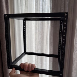 Può includere: Un telaio per server rack a forma di cubo, aperto e di colore nero, realizzato in metallo. La struttura presenta binari verticali con una serie di fori di montaggio circolari regolarmente distanziati, collegati da barre di supporto orizzontali.