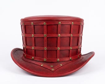 May include: A deep red top hat featuring a structured grid pattern of leather straps across the crown. The intersection points of the grid are accented with small, round, metallic brass-colored studs. The brim is curved and matches the red color.