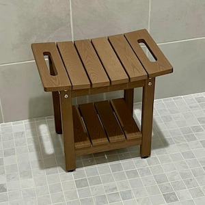 May include: A brown wooden shower bench with a slatted seat and a lower shelf. The bench has a rectangular shape with cut-out handles on each side. The bench is approximately 18 inches long, 12 inches wide, and 18 inches tall.