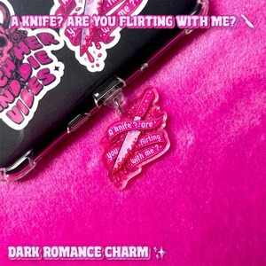 Può includere: Un ciondolo in acrilico rosa con un design a coltello e la scritta "A knife? Are you flirting with me?" Il ciondolo è attaccato a una custodia per telefono nera con adesivi. Le parole "Dark Romance Charm" sono in basso.