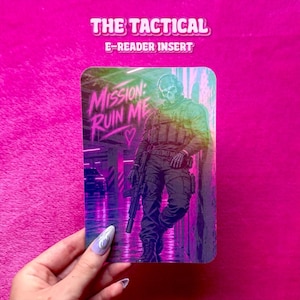 Könnte beinhalten: Ein rechteckiger E-Reader-Einsatz mit einer Grafik eines Soldaten, der eine Totenkopfmaske und taktische Ausrüstung trägt und ein Gewehr hält. Der Text MISSION: RUIN ME und ein Herzsymbol sind in Neonpink vor einem dunklen Parkhaus-Hintergrund gedruckt.