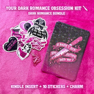 Puede incluir: Un paquete rosa con el texto "YOUR DARK ROMANCE OBSESSION KIT" incluye una inserción de Kindle, pegatinas y un dije. Las pegatinas presentan frases como "I like my men tall, dark &" y "A knife? are you flirting with me?"
