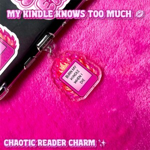 May include: A pink acrylic charm with the text "BURN MY KINDLE WHEN I DIE" on a pink rectangle, surrounded by flames. The charm is attached to a black phone case. The words "MY KINDLE KNOWS TOO MUCH" and "CHAOTIC READER CHARM" are also visible.