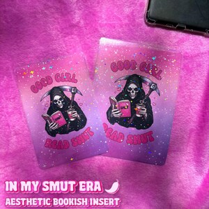 Può includere: Due inserti estetici per libri con uno sfondo sfumato rosa e viola. Ogni inserto presenta un'illustrazione della Morte che legge un libro con la parola "SMUT", tenendo una tazza di caffè. Il testo "GOOD GIRL READ SMUT" è sopra e sotto l'illustrazione. Il testo "IN MY SMUT ERA" è in basso.