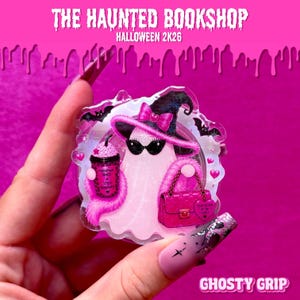 May include: A clear acrylic phone grip featuring a ghost wearing a black witch hat with a pink bow and black sunglasses. The ghost holds a pink cup labeled Pumpkin Spice & Spice Romance and carries a quilted pink handbag with a heart-shaped tag.