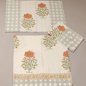 Könnte beinhalten: Weißes Tischwäsche-Set mit floralem Druck. Das Set beinhaltet eine Tischdecke, zwei Tischsets und eine Serviette. Jedes Teil hat ein großes orangefarbenes Blumendesign mit grünen Blättern und einem grauen geometrischen Rand.