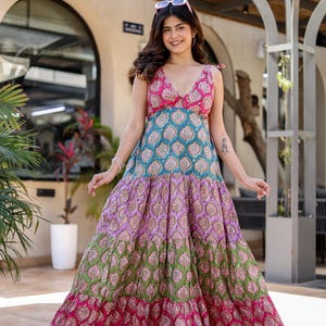 Puede incluir: Un vestido largo escalonado y colorido con escote en V. El vestido presenta un corpiño con estampado floral rosa y turquesa, que se transforma en capas verdes y moradas, y una última capa rosa en el dobladillo. El vestido sin mangas parece estar hecho de tela ligera.