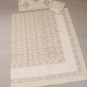 Könnte beinhalten: Ein cremefarbenes Tischdecken-Set mit passendem Platzset und Serviette. Die Tischdecke hat ein sich wiederholendes Blumenmuster in Hellbraun. Platzset und Serviette haben ein Blumendesign und einen geometrischen Rand.