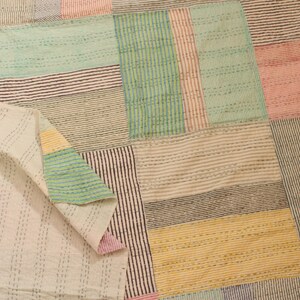 Könnte beinhalten: Ein Patchwork-Quilt mit einer Vielzahl von Farben und Mustern. Der Quilt besteht aus rechteckigen Blöcken in Rosa-, Grün-, Blau-, Gelb- und Weißtönen. Jeder Block hat ein anderes Streifendesign, und der Quilt ist in der Ecke gefaltet.