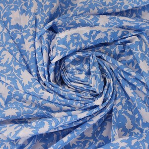 Könnte beinhalten: Nahaufnahme eines Stoffes mit einem sich wiederholenden Blumenmuster. Der Stoff ist hellblau mit weißen Blumendesigns. Der Stoff ist gerafft und gewirbelt, wodurch ein strukturierter Effekt entsteht.