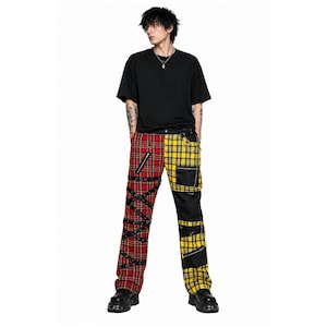 May include: A person wearing a black t-shirt and two-tone plaid pants. The pants are red and yellow with black accents, zippers, and straps. The person is also wearing black boots.
