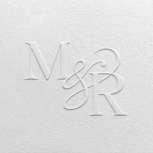 Op de afbeelding: Een wit gestructureerd papieren oppervlak met een in reliëf gedrukt monogram van de letters M en R verbonden door een ampersand. De letters zijn weergegeven in een klassiek schreeflettertype met een subtiel schaduweffect voor een tactiel uiterlijk.