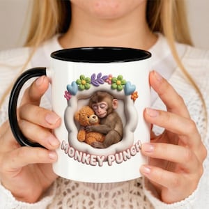 May include: White ceramic mug with a black handle and rim. The mug features a cartoon illustration of a monkey hugging a teddy bear, surrounded by flowers and hearts. The text "MONKEY PUNCH" is printed below the illustration.