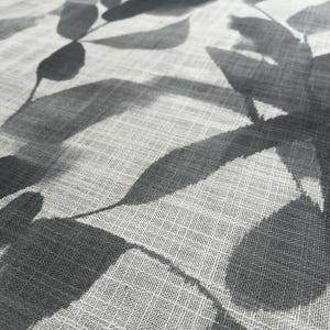 May include: Close-up of a light-colored fabric with a repeating pattern of gray leaves. The leaves have a watercolor effect, with varying shades of gray. The fabric has a subtle, textured appearance.