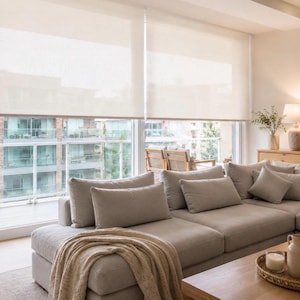 Puede incluir: Dos cortinas enrollables de color blanco roto instaladas sobre grandes ventanales de cristal. Las cortinas están hechas de un tejido semitransparente que permite la entrada de luz suave y difusa, manteniendo un aspecto limpio y sencillo.