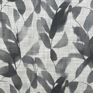 May include: A fabric with a repeating pattern of stylized leaves in shades of gray and black against a light gray background. The leaves have a watercolor effect, creating a soft, textured appearance. The fabric has a linen-like weave.