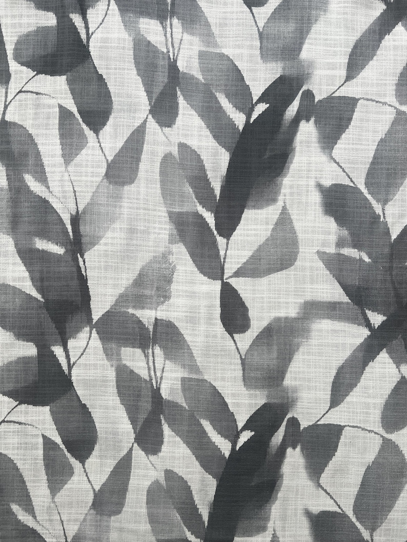 May include: A fabric with a repeating pattern of stylized leaves in shades of gray and black against a light gray background. The leaves have a watercolor effect, creating a soft, textured appearance. The fabric has a linen-like weave.