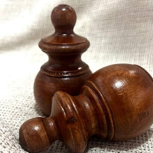 May include: Two turned wooden finials in a warm brown colour. One finial stands upright, while the other lies on its side, showcasing the detailed craftsmanship. The finials have a classic, decorative design, perfect for home decor projects.