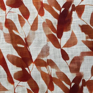 May include: Close-up of a fabric with a repeating pattern of stylized leaves. The leaves are in shades of reddish-brown and orange, with a watercolor effect. The background is a light, textured off-white.