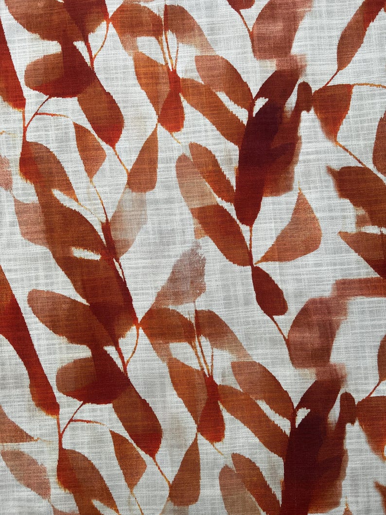 May include: Close-up of a fabric with a repeating pattern of stylized leaves. The leaves are in shades of reddish-brown and orange, with a watercolor effect. The background is a light, textured off-white.