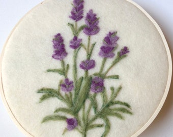 May include: A needle felted lavender flower arrangement in a wooden embroidery hoop. The flowers are purple and the stems are green.