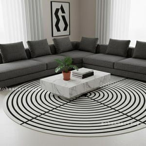 May include: A modern living room setup featuring a large gray sectional sofa with multiple cushions. A marble-look coffee table holds books and a potted plant. A black and white circular rug and artwork complete the contemporary design.