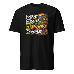 May include: A black short-sleeve t-shirt featuring a graphic print with the text EAT SLEEP MADEIRA REPEAT. The design includes icons for eating and sleeping, a coastal landscape scene with a sunset, a glass of wine, and tropical flowers.