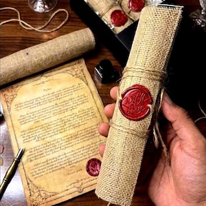 May include: A rolled parchment scroll wrapped in tan burlap twine and secured with a circular red wax seal featuring the embossed text With Love. An unrolled piece of aged paper with printed cursive text and a red wax seal lies nearby.