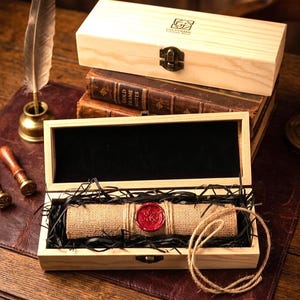 May include: A wooden box with a hinged lid, containing a rolled scroll sealed with red wax. The box sits atop a stack of books and a leather surface. A feather quill and inkwell are also visible.