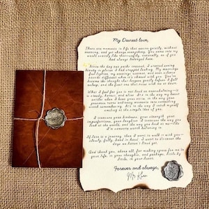 Op de afbeelding: Een donkerbruine envelop vastgebonden met touw en een waszegel naast een vel crèmekleurig perkamentpapier met verbrande randen. Het papier bevat handgeschreven tekst die begint met "My Dearest love," en een waszegel met een bloemmotief.