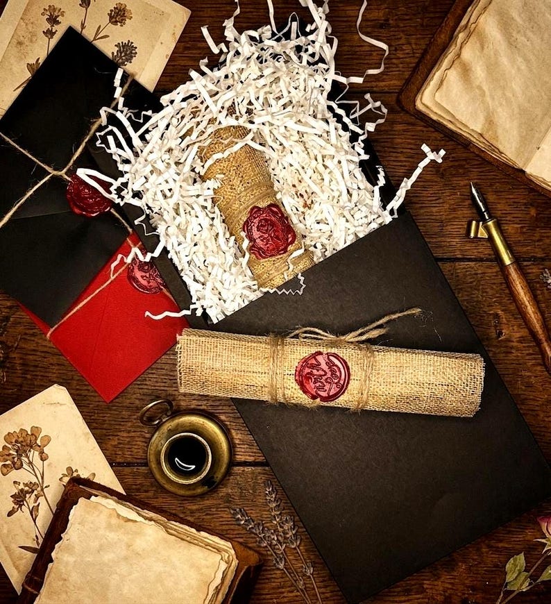 K&ouml;nnte beinhalten: Eine rustikale Szene mit einer schwarzen Box, die einen mit Jute umwickelten Gegenstand enth&auml;lt, der mit rotem Wachs versiegelt ist. Eine Schriftrolle, Umschl&auml;ge, eine kleine Tasse und ein Stift sind ebenfalls vorhanden, alles auf einer Holzoberfl&auml;che angeordnet.