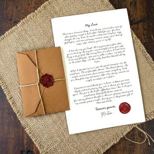 Puede incluir: Una carta blanca titulada My Love con texto negro en cursiva, acompañada de un sobre marrón atado con cuerda y un sello de cera roja. Un sello de cera roja a juego se encuentra en la parte inferior derecha de la carta sobre tela de arpillera.