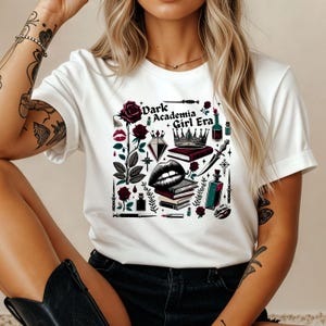 K&ouml;nnte beinhalten: Wei&szlig;es T-Shirt mit einem grafischen Design mit einer Rose, Lippen, einer Krone, B&uuml;chern und dem Text "Dark Academia Girl Era". Das Design enth&auml;lt dunkelrote, schwarze und gr&uuml;ne Elemente.