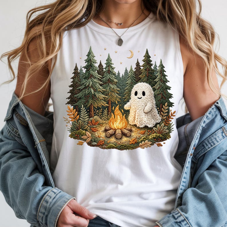 May include: White tank top featuring a whimsical illustration of a friendly ghost sitting by a campfire in a forest. The design includes tall green pine trees, autumn leaves, a crescent moon, and stars. The ghost is a light beige color.