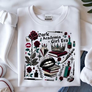 K&ouml;nnte beinhalten: Wei&szlig;es Sweatshirt mit einem Grafikdesign mit dem Text "Dark Academia Girl Era". Das Design umfasst Rosen, eine Krone, B&uuml;cher, einen Diamanten, Lippen und andere gotisch inspirierte Elemente in Rot, Schwarz und Gr&uuml;n.