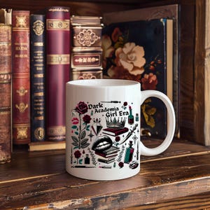 K&ouml;nnte beinhalten: Wei&szlig;e Keramiktasse mit dem Text "Dark Academia Girl Era" und Illustrationen von Rosen, B&uuml;chern und einer Krone. Die Tasse steht vor einer Sammlung antiker B&uuml;cher auf einem Holzregal.