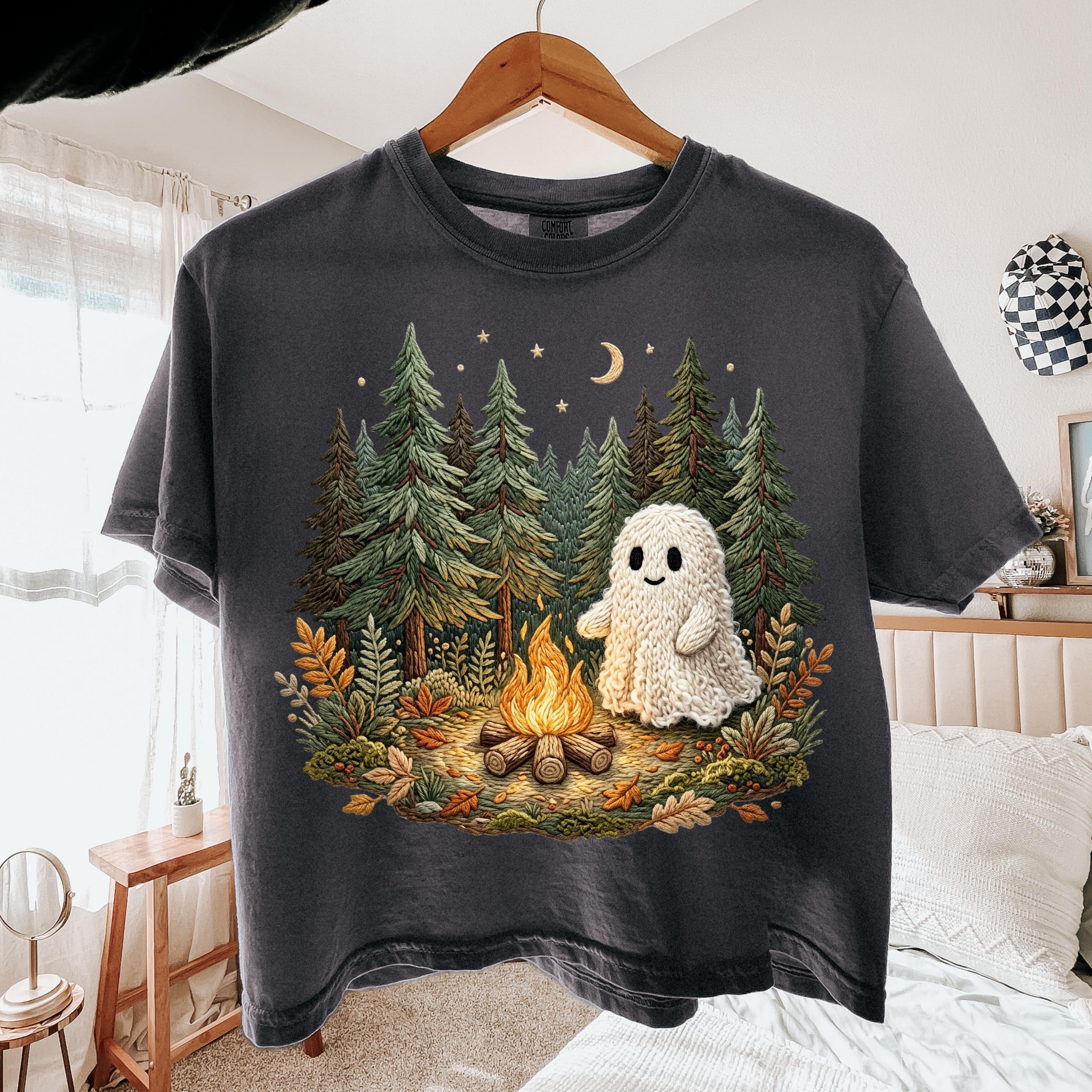 May include: Dark gray t-shirt featuring a whimsical illustration of a friendly ghost near a campfire in a forest setting. The design includes trees, a crescent moon, and stars, creating a cozy, outdoorsy theme.