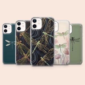 May include: Five smartphone cases arranged in a row, each featuring a unique dragonfly design. The cases display various artistic styles, including gold-lined dragonfly patterns on dark backgrounds, watercolor-style floral motifs, and minimalist illustrations.