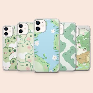 May include: A collection of five phone cases with various frog-themed designs. The cases feature different patterns, including repeating frog faces, frogs with flowers, and frogs on a blue background. The cases are in clear protective cases.