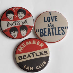 May include: Three vintage Beatles fan club badges. One badge reads "I love the Beatles" in navy blue text. Another badge says "I'm a Beatles Fan" with images of the band members. The third badge says "Member Beatles Fan Club".