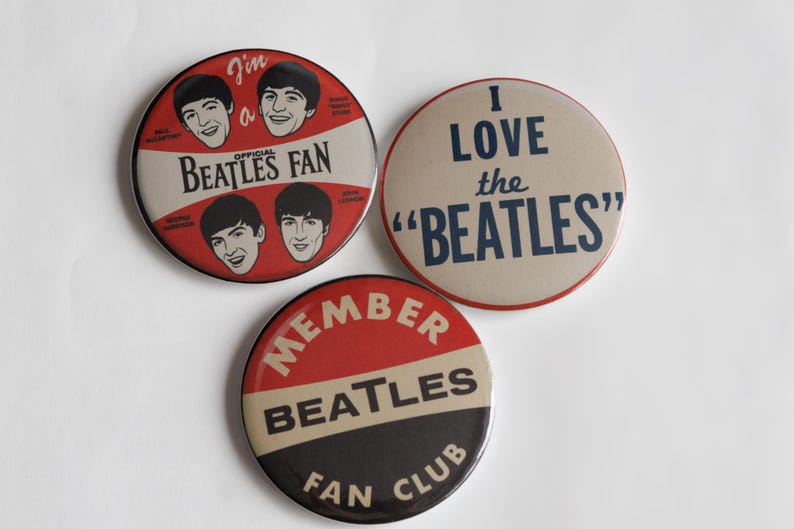 May include: Three vintage Beatles fan club badges. One badge reads "I love the Beatles" in navy blue text. Another badge says "I'm a Beatles Fan" with images of the band members. The third badge says "Member Beatles Fan Club".