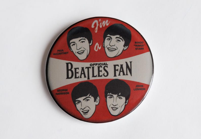 May include: A circular badge with a red and white design, featuring illustrations of The Beatles. The badge includes the text "I'm a Beatles Fan" and portraits of Paul McCartney, John Lennon, George Harrison, and Ringo Starr.