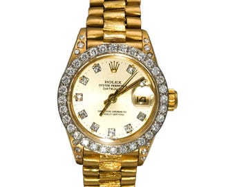 May include: A gold Rolex Oyster Perpetual Datejust watch with a diamond-encrusted bezel and hour markers. The watch features a gold dial with the Rolex logo and a date display at the 3 o'clock position. The watch band is also gold.