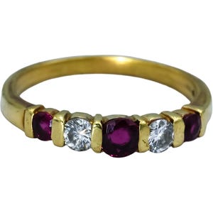 Op de afbeelding: Een gouden ring met een rij van vijf afwisselend geplaatste, rond geslepen edelstenen. De zetting bevat drie dieprode robijnen en twee heldere witte diamanten, vastgezet in een gepolijste geelgouden ringband.
